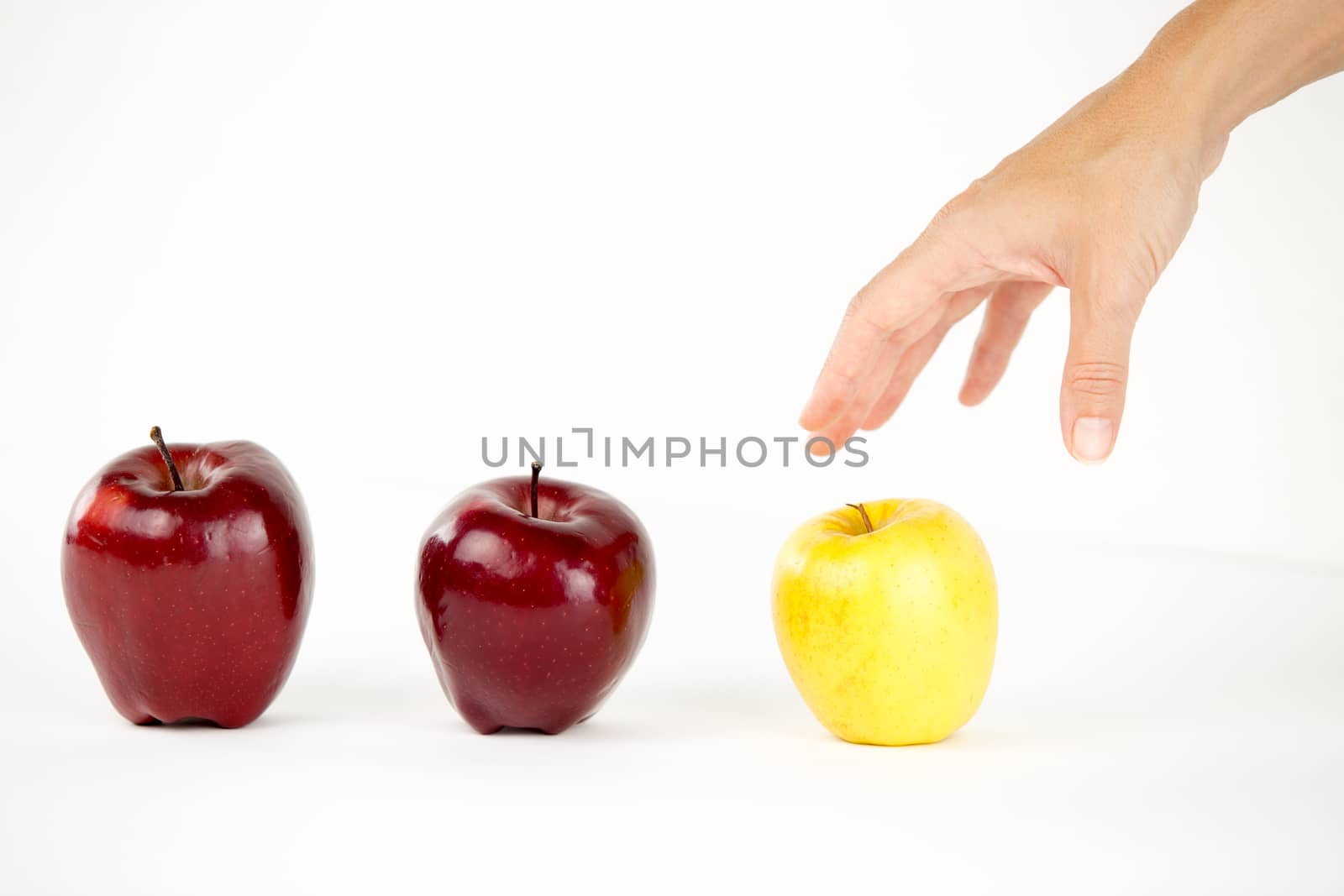 Concept of diversity: a woman's hand is about to grab the only yellow apple among the other red ones