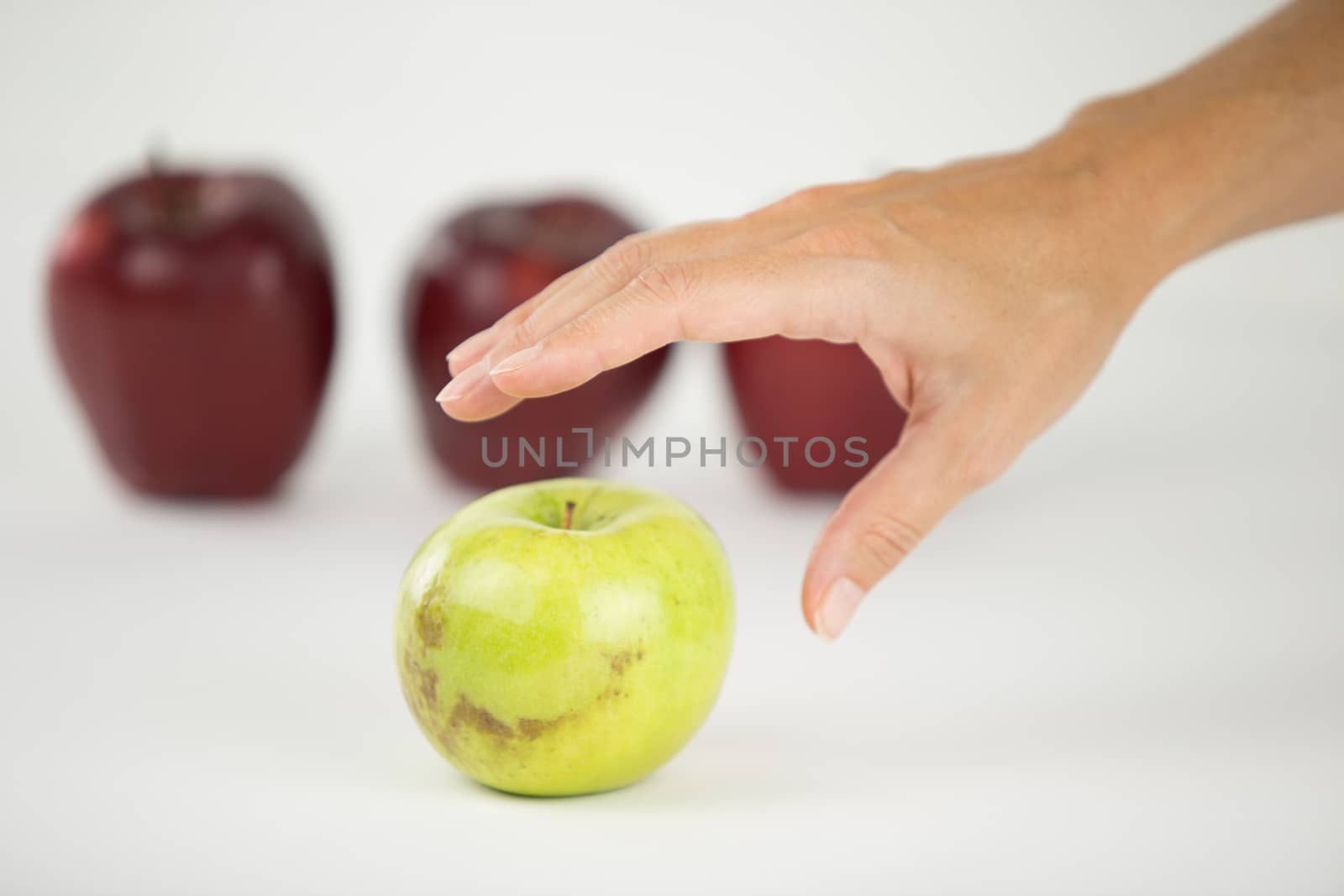 Concept of diversity: a woman's hand is about to grab the only green apple among the other red ones by robbyfontanesi