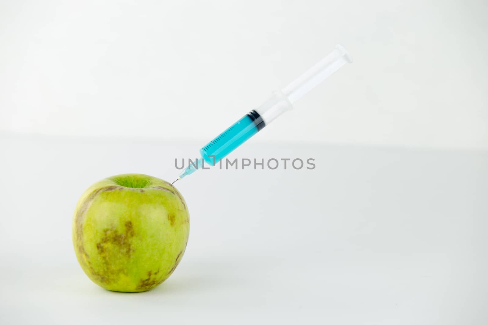 Concept: human GMO manipulation of nature and relative poisoned fruits. Close-up of an apple contaminated with a syringe threaded in and white background by robbyfontanesi