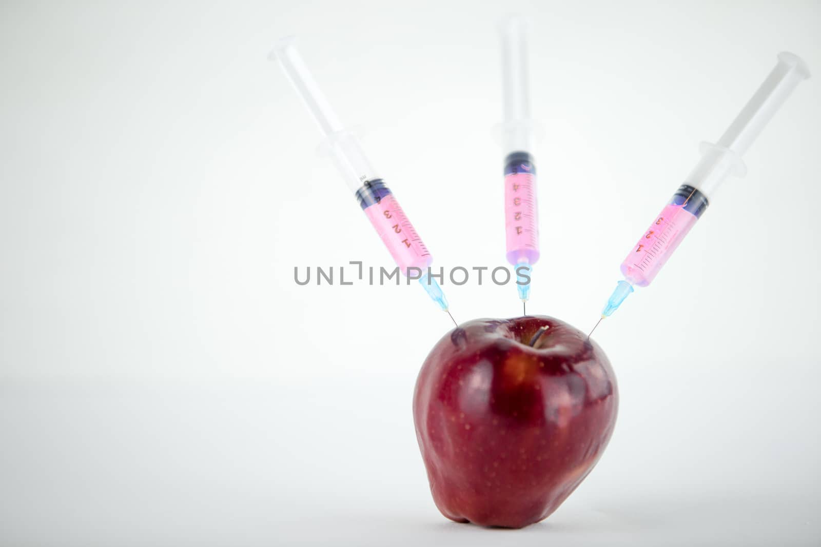 Concept: human GMO manipulation of nature and relative poisoned fruits. Close-up of an apple contaminated with three syringes threaded in and white background