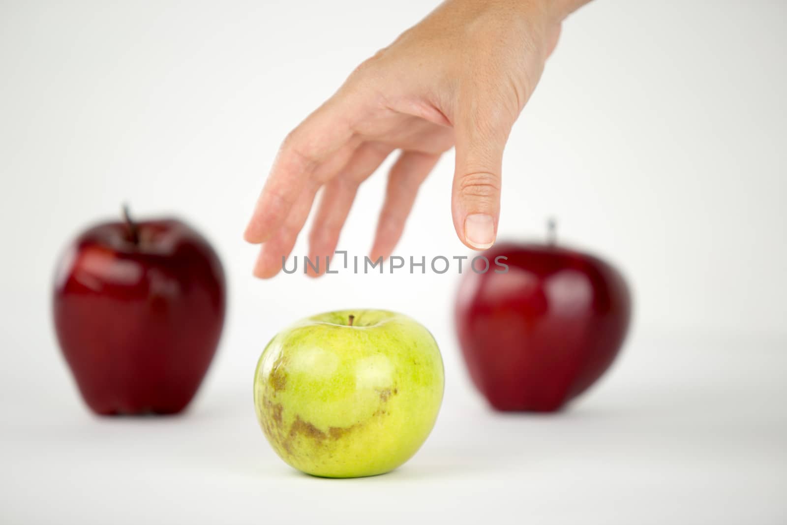 Concept of diversity: a woman's hand is about to grab the only green apple among the other red ones by robbyfontanesi