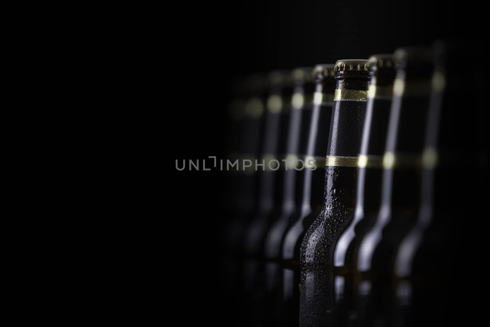 Beer bottles with blank labels lined up in selective focus on black background, one with frost droplets