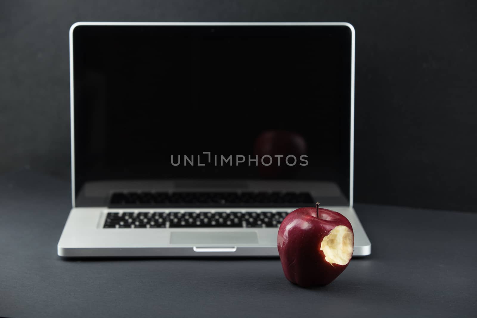Shiny red apple resting on an open aluminum laptop in selective focus on a black background