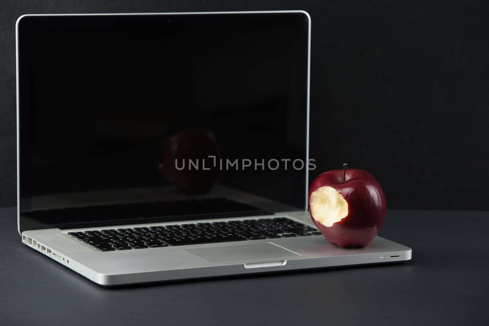 Shiny red apple resting on an open aluminum laptop in selective focus on a black background