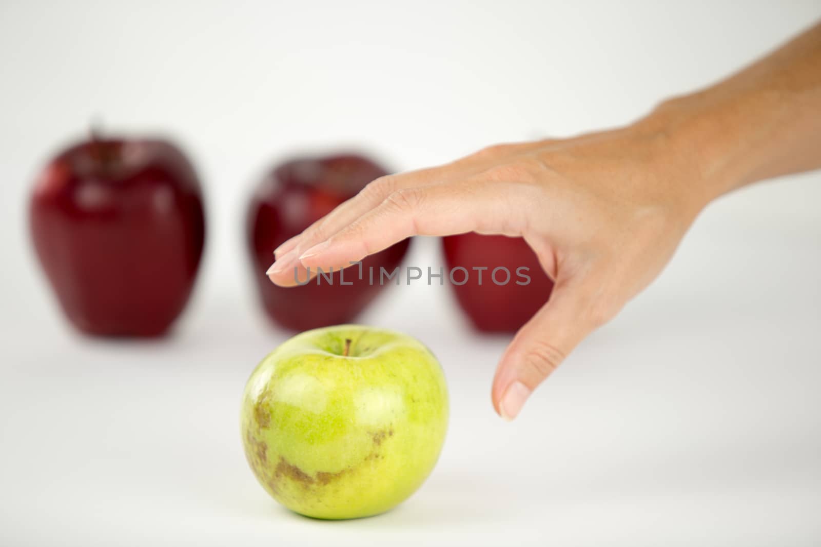 Concept of diversity: a woman's hand is about to grab the only green apple among the other red ones