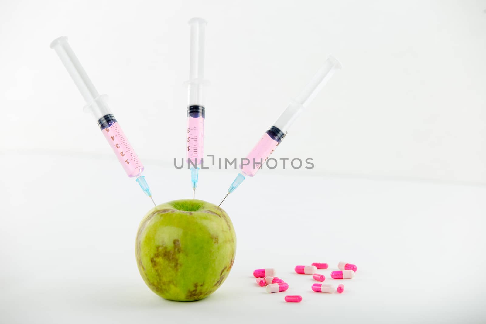 Concept: human GMO manipulation of nature and relative poisoned fruits. Close-up of an apple contaminated with three syringe threaded in and medicines on a white background by robbyfontanesi