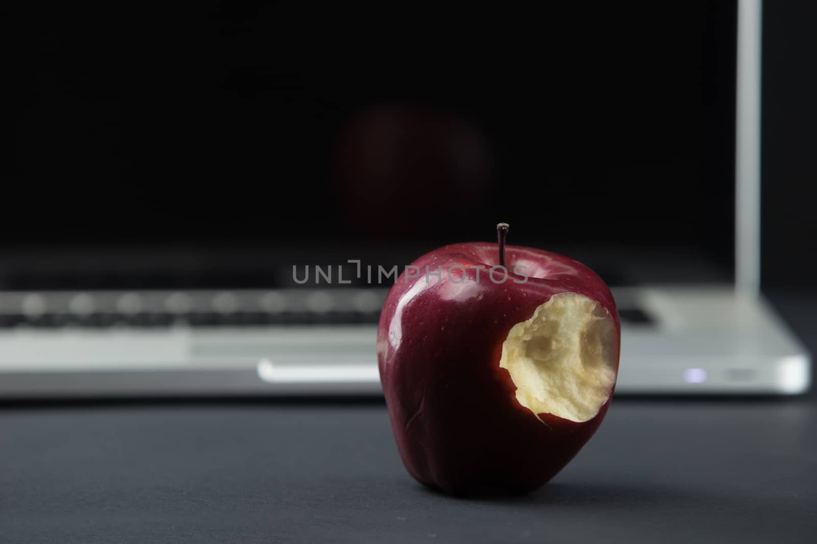 Shiny red apple resting on an open aluminum laptop in selective focus on a black background