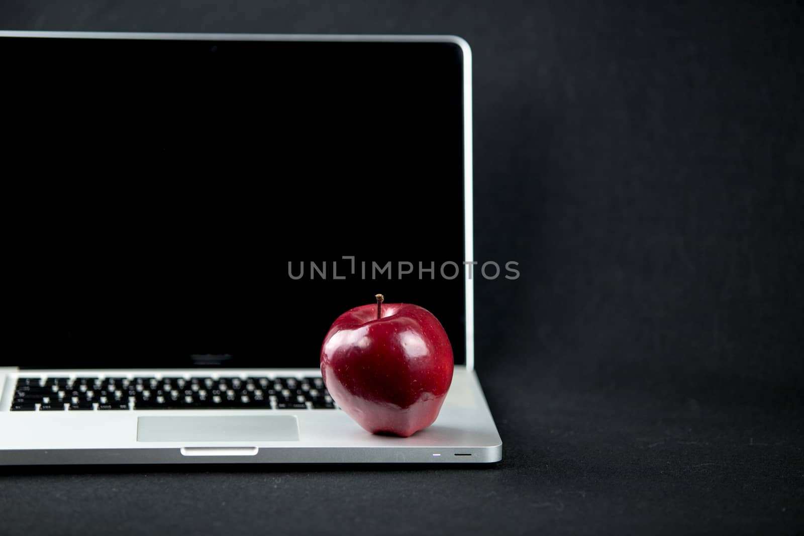 Shiny red apple resting on an open aluminum laptop in selective focus on a black background