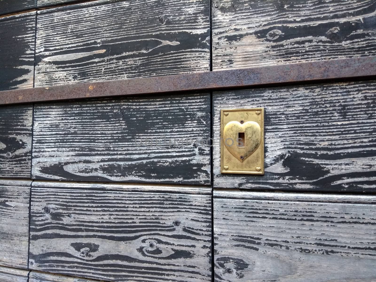 Concept: love never gets old. An old wooden door discolored by time with the heart-shaped brass lock by robbyfontanesi