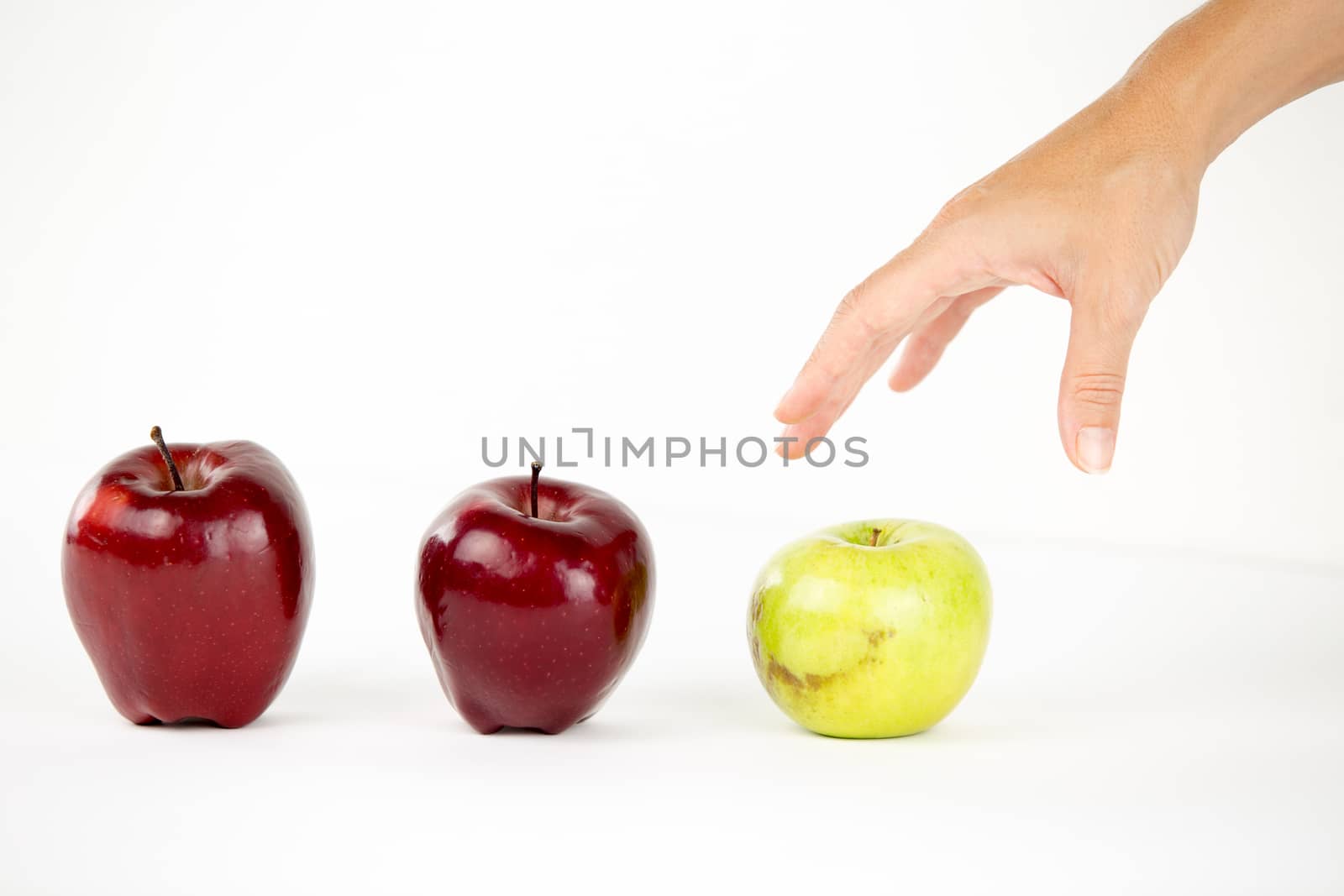 Concept of diversity: a woman's hand is about to grab the only green apple among the other red ones by robbyfontanesi