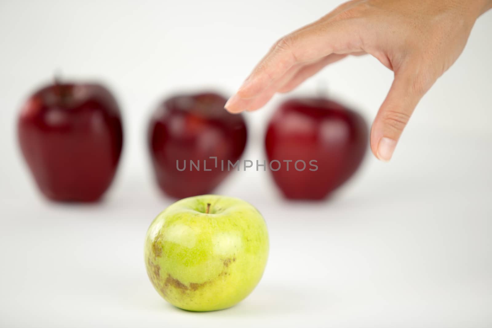 Concept of diversity: a woman's hand is about to grab the only green apple among the other red ones