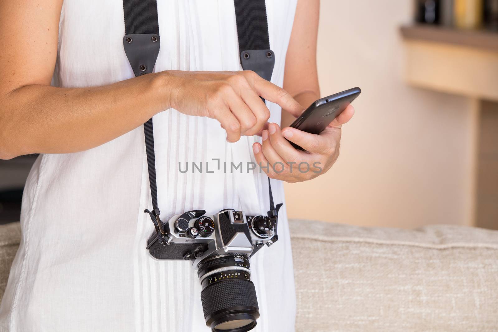 Contrast between old and modern times: a young woman with a vintage camera around her neck fiddles with her smartphone