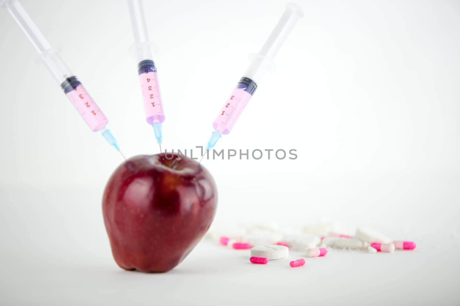 Concept: human GMO manipulation of nature and relative poisoned fruits. Close-up of an apple contaminated with three syringe threaded in and medicines on a white background by robbyfontanesi