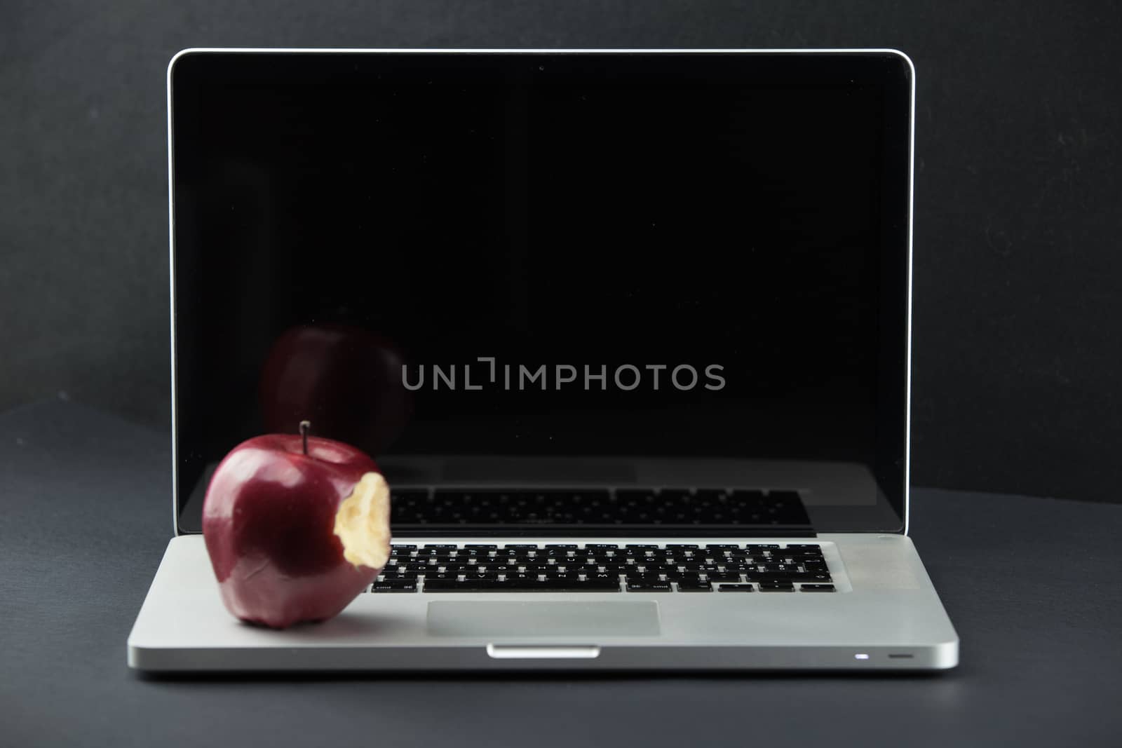 Shiny red apple resting on an open aluminum laptop in selective focus on a black background