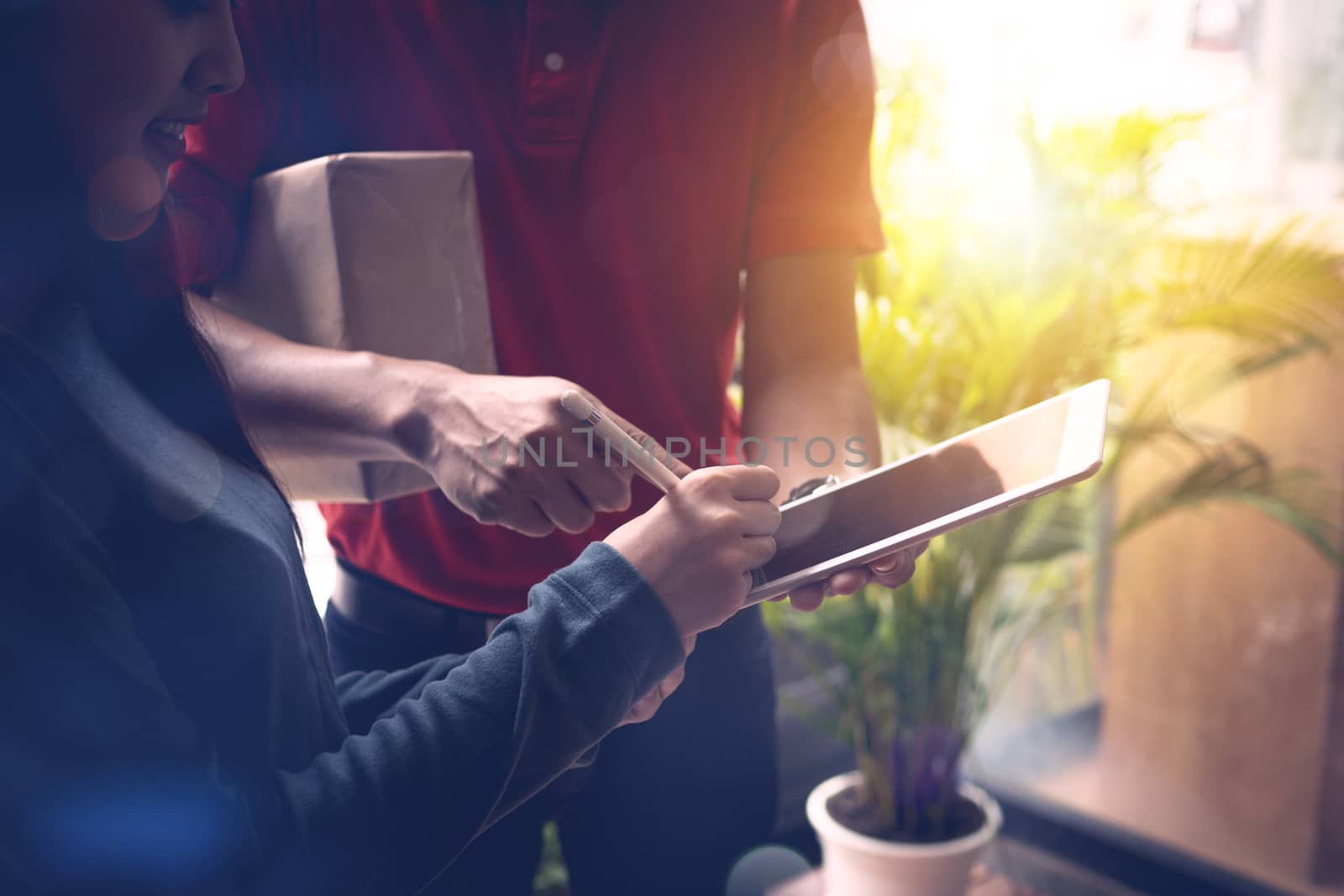 Beautiful girl receiving parcel from postman and signing on tablet that delivery goods to home's customer