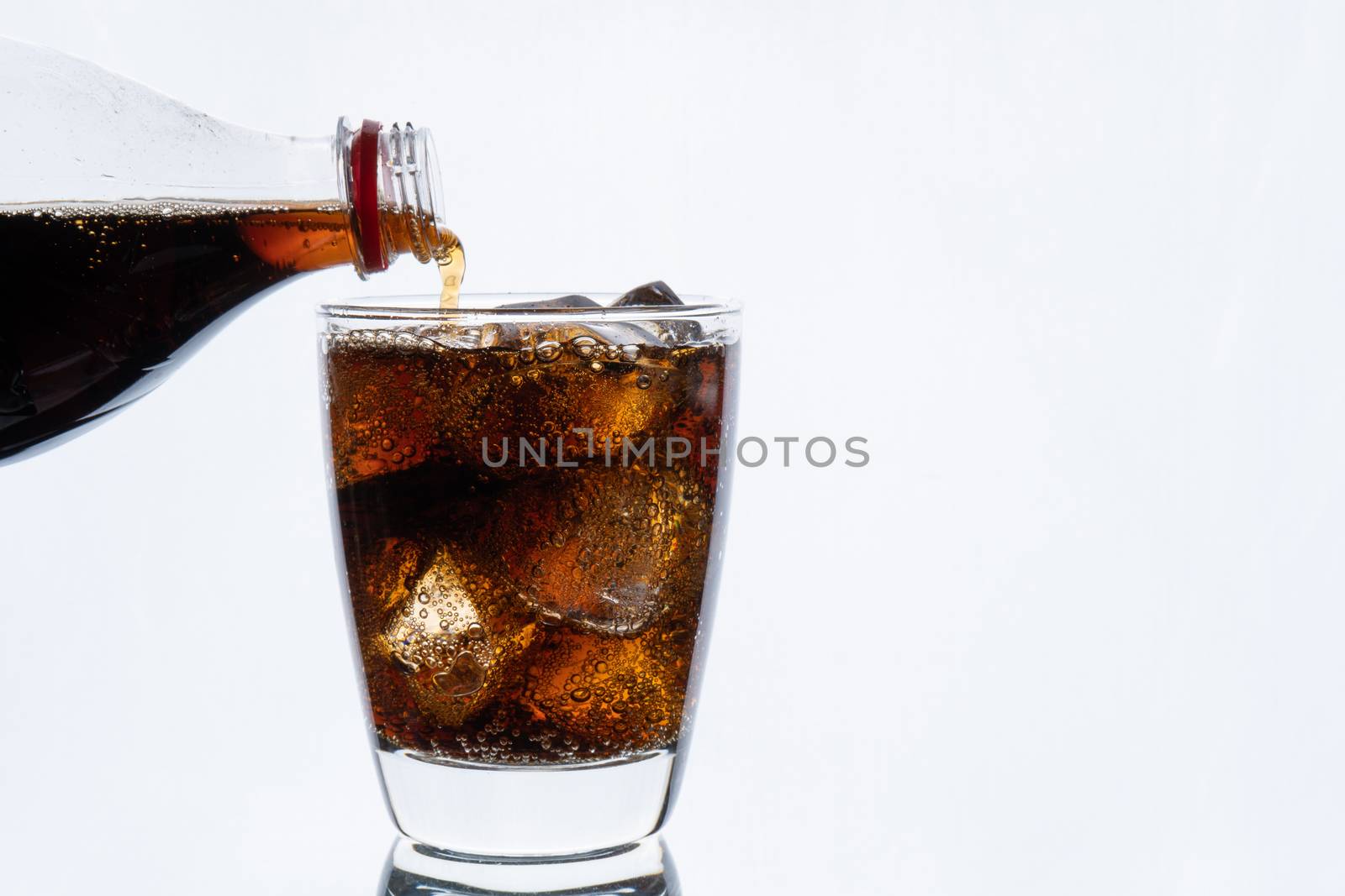 Cold drinking, pouring soda from bottle, glass of cola with ice for hot and summer drink isolated on white background
