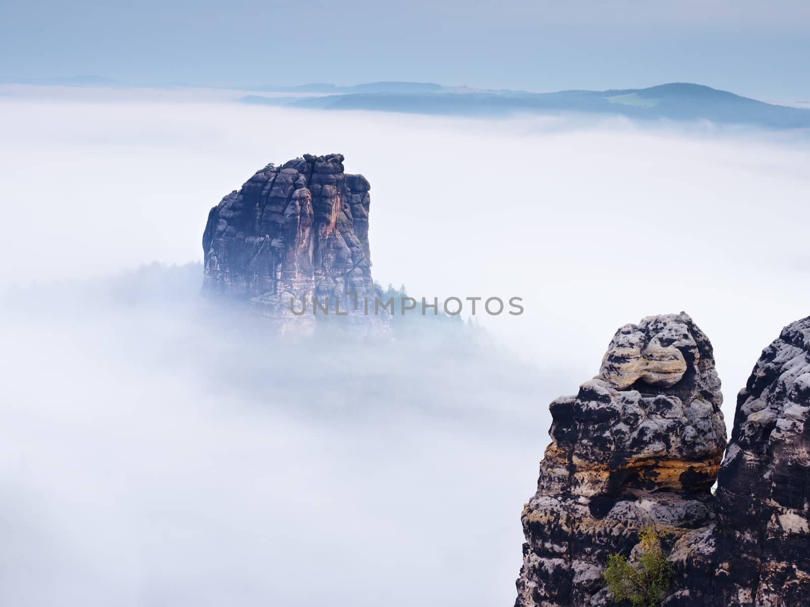 Sharp sandstone rock empire sticking out from heavy fog. Deep misty valley full of creamy mist. Popular climbers resort in autumn look
