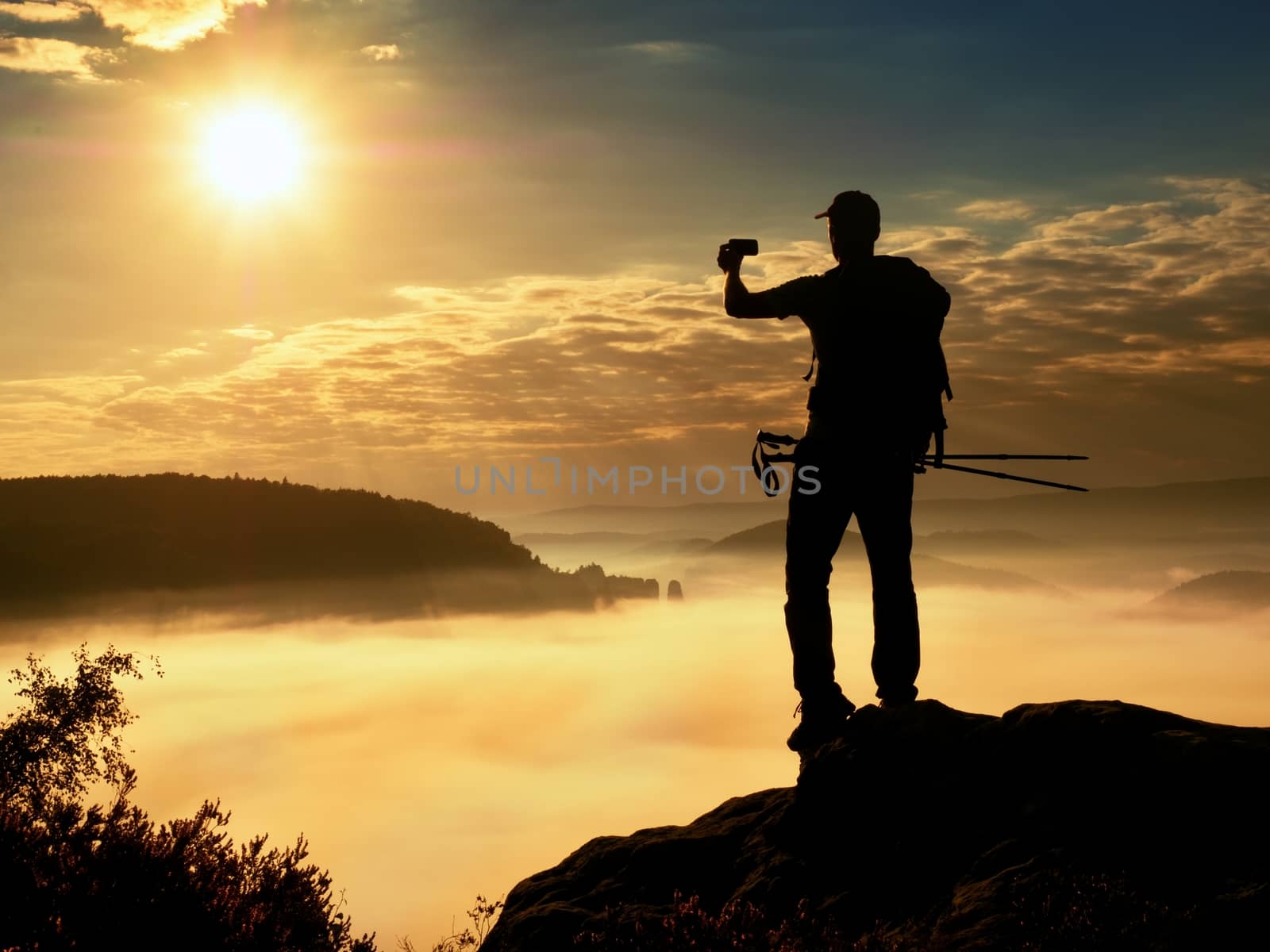 Strong man hiker taking photo with smart phone at mountain peak. by rdonar2