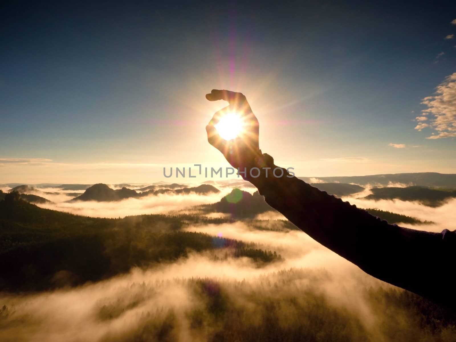 Man hand touch Sun. Misty daybreak in a beautiful hills. Peaks of hills are sticking out from foggy background, the fog is red and orange due to Sun rays.  Lens defects.