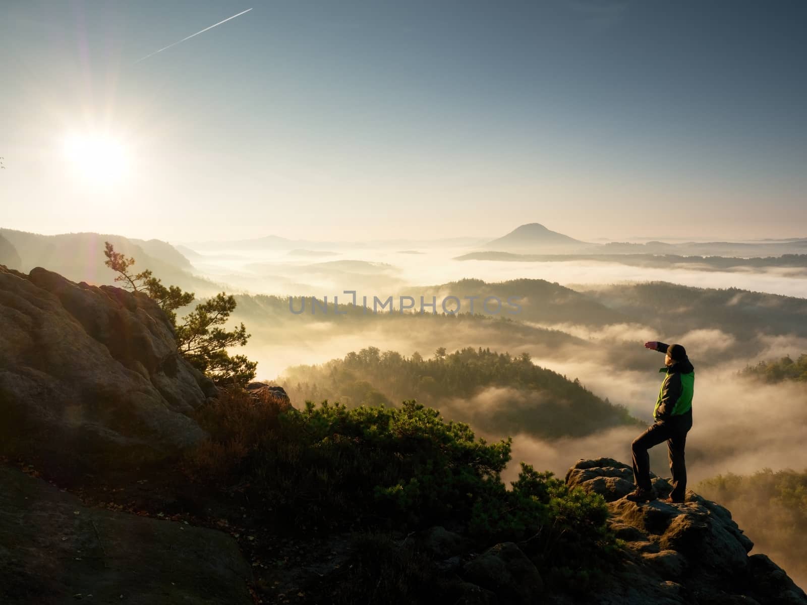 Man silhouette stay on sharp rock peak. Satisfy hiker enjoy view. Tall man on rocky cliff watching down to landscape. Vivid and strong vignetting effect.