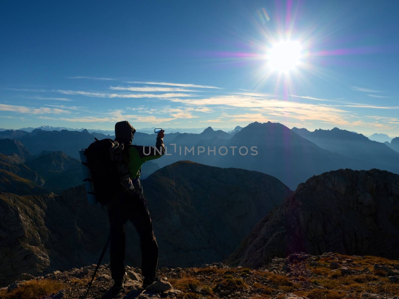 Hiker takes phone photo. Man on Alps mountain peak.View to blue foggy valley by rdonar2