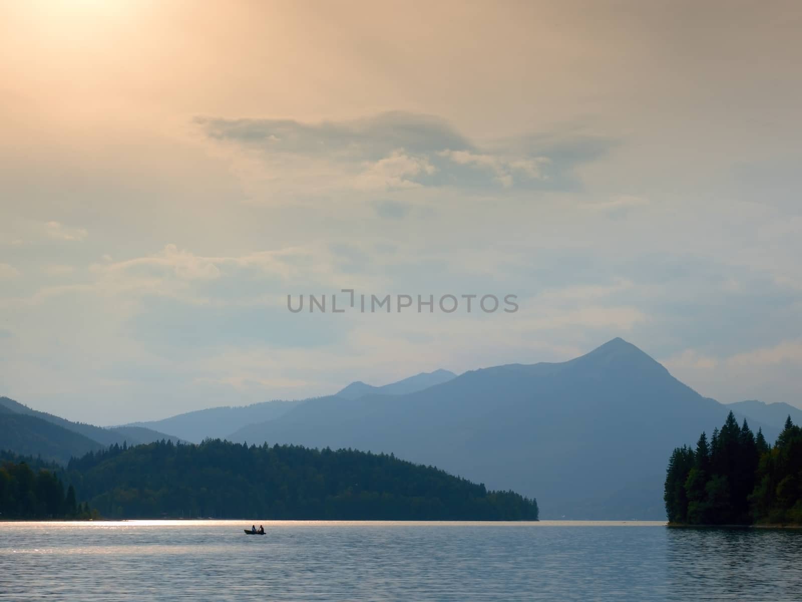 Abandoned fishing paddle boat on Alps lake. Evening lake glowing by sunlight.  by rdonar2