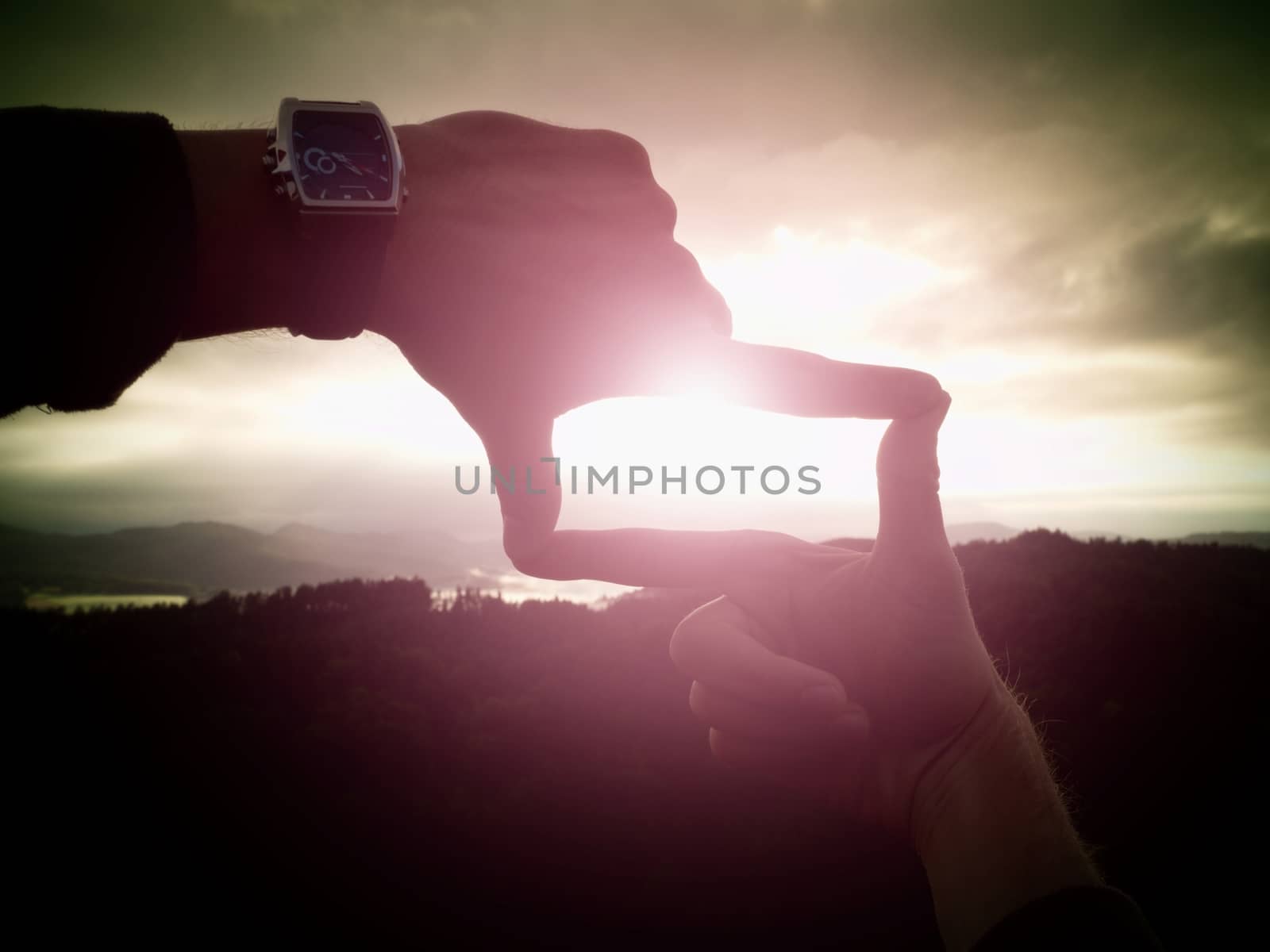 Close up of hands with watch making frame gesture. Dark misty valley bellow in landscape. Sunny autumn daybreak in mountains.