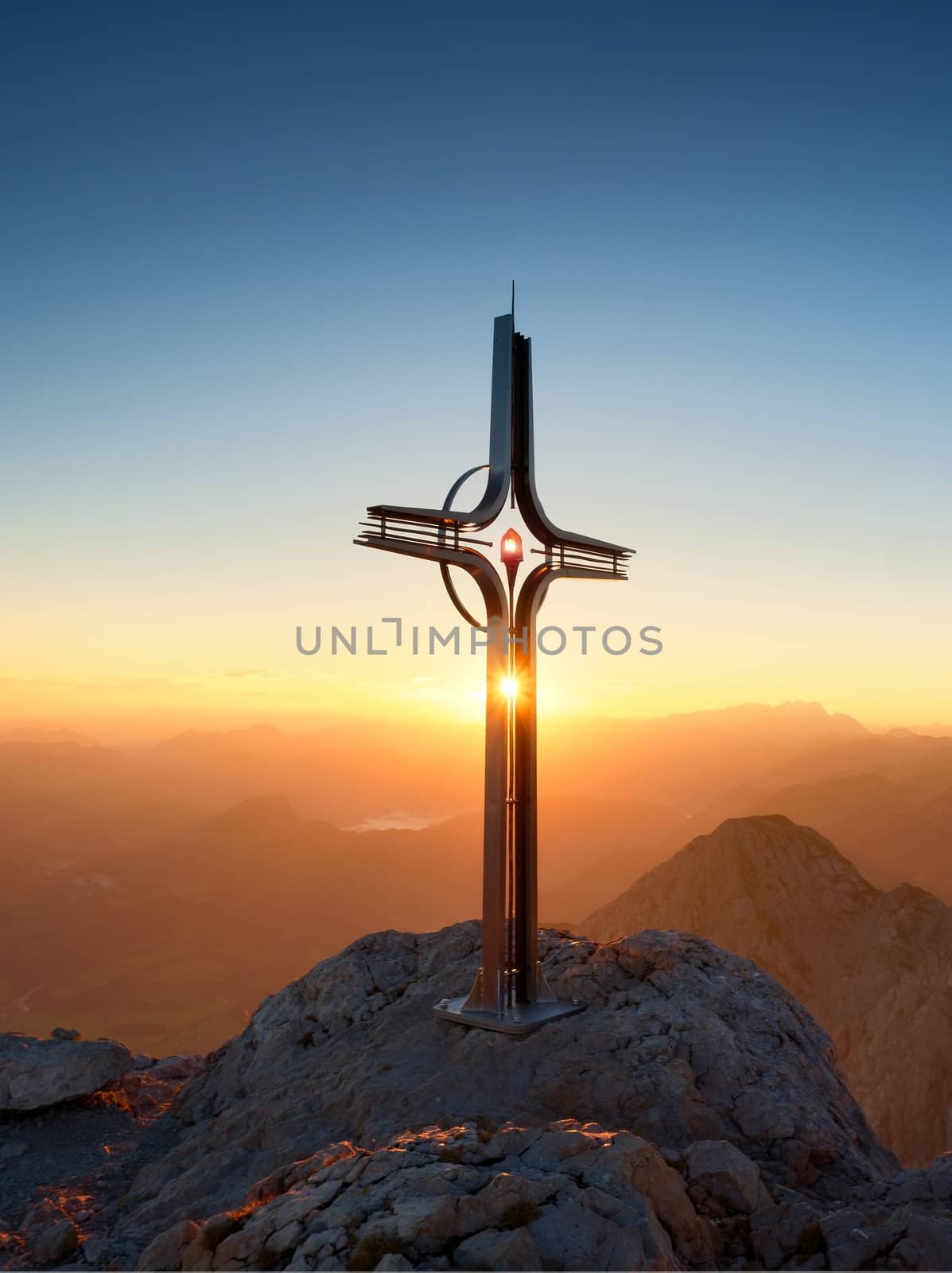 Steel crucifix at mountain peak in Alps. Sharp rocky summit, daybreak Sun in sky.  by rdonar2