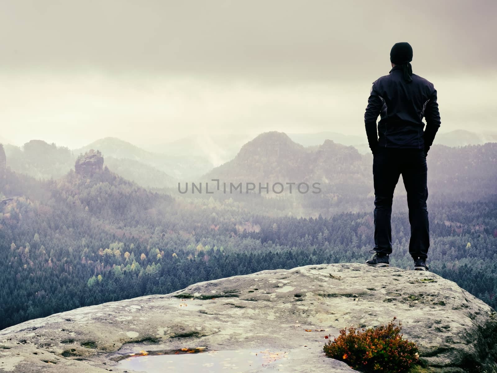 Tall man in black on cliff and watch to mountain sunrise.Silhouette in selfconfident pose. Dark silhouette of rocks.