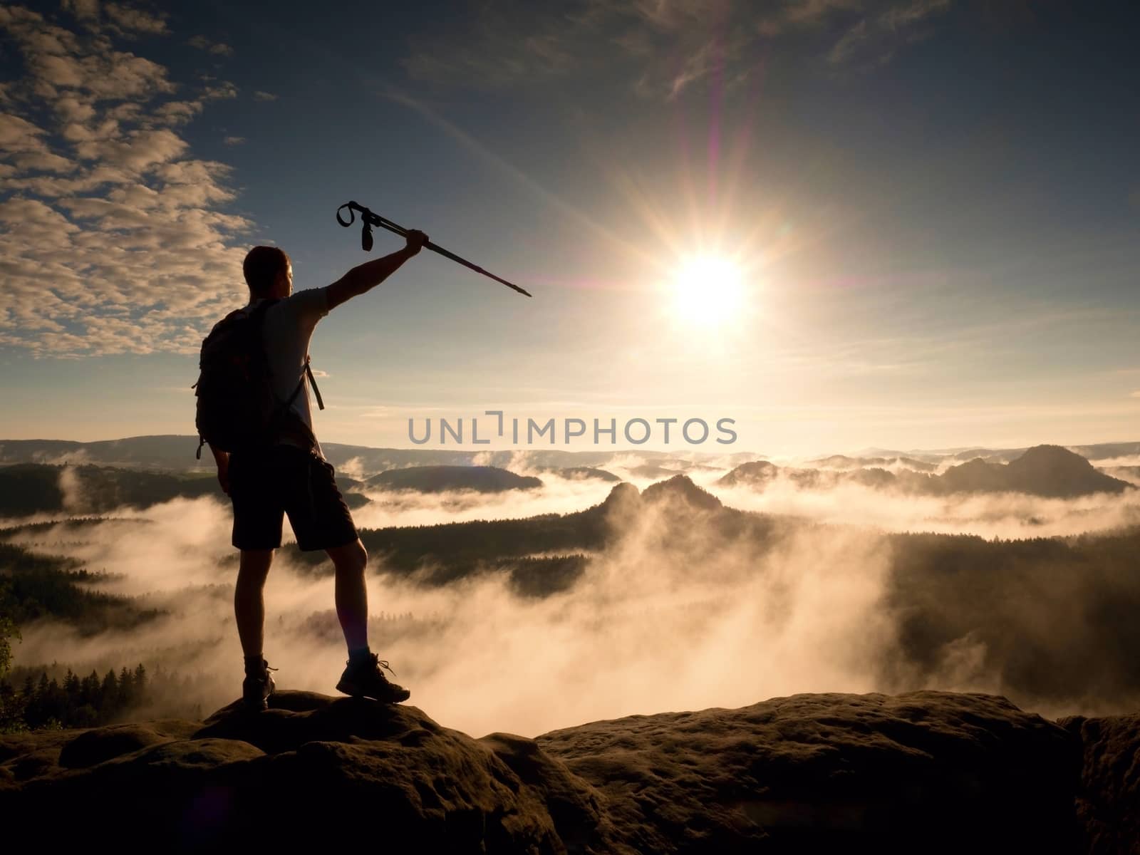 Hiker with sporty backpack on rocky view point above misty valley. Sunny daybreak by rdonar2