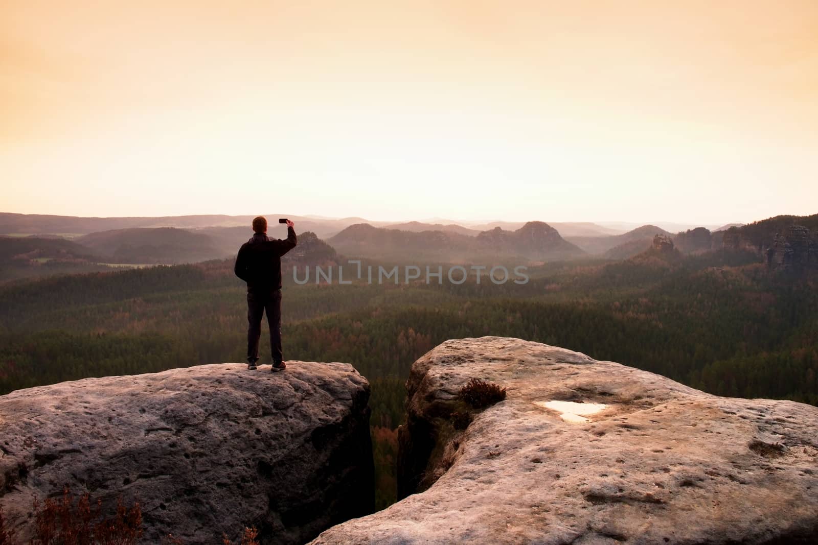 Hiker photography sunrise by smart phone. Man stay on peak of rock by rdonar2