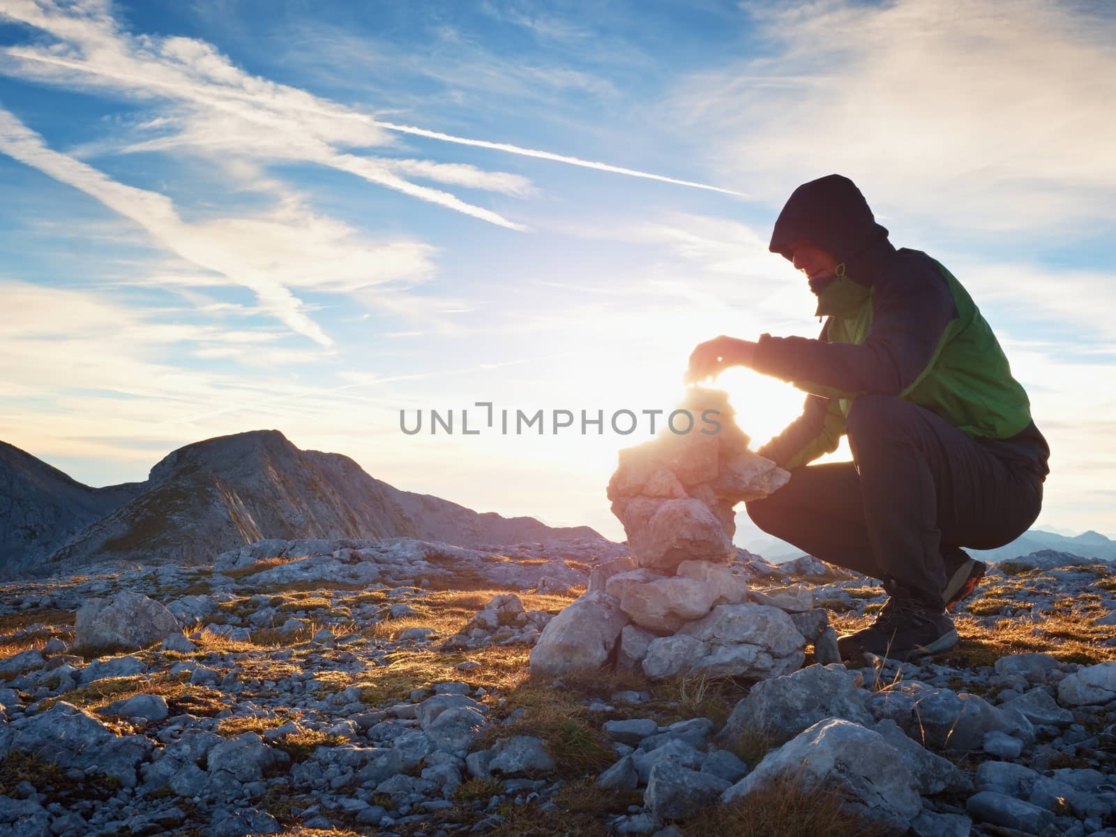 Alone hiker man on the top of the Alpine mountain building pyrmid from pebbles. Mans hand hold the last stone for the pyramid.  Stones on Alps mountain gravel summit. 