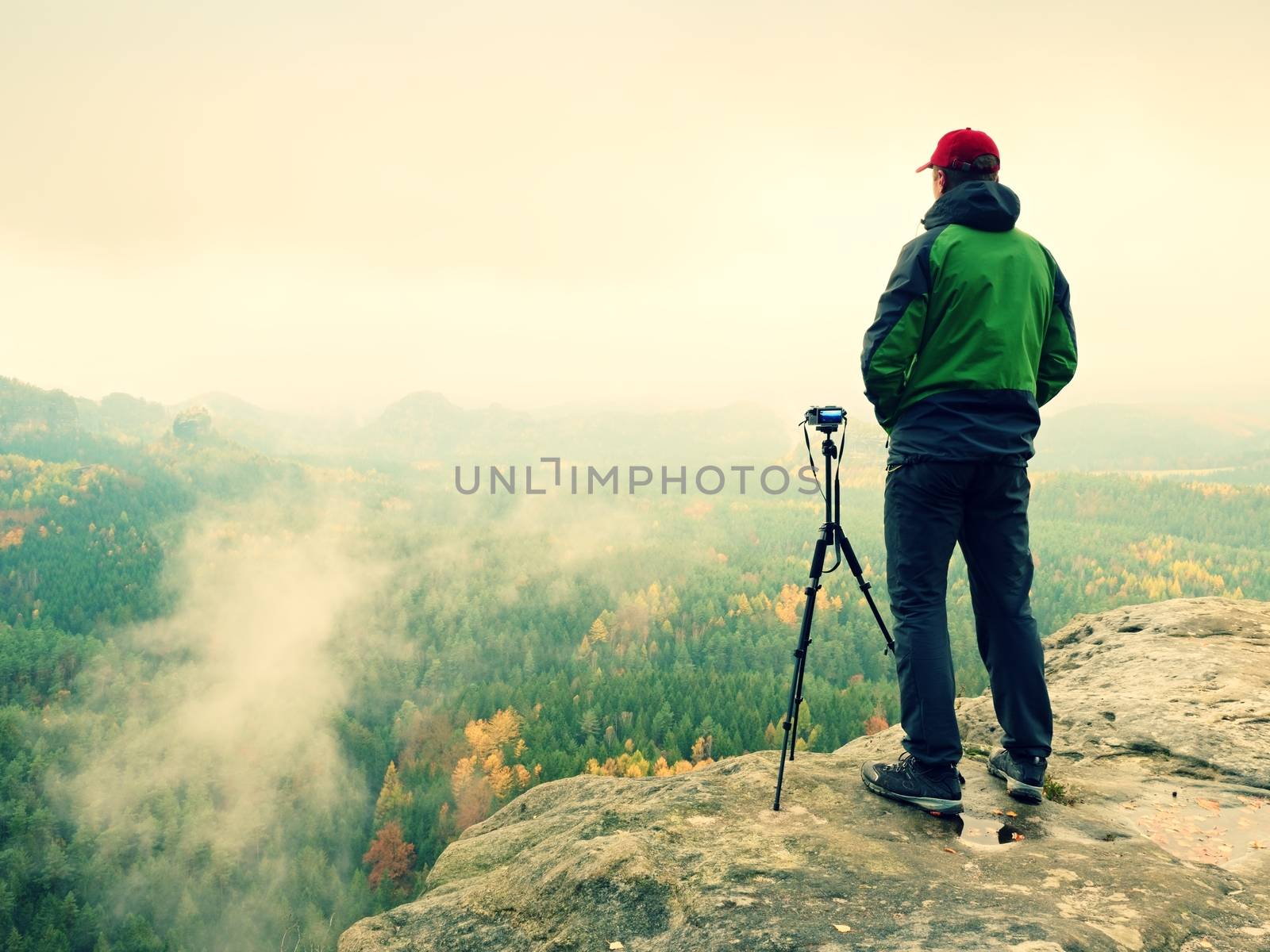 Nature photographer stay at tripod with mirror camera on peak of rock. Dreamy fogy landscape, spring orange pink mist