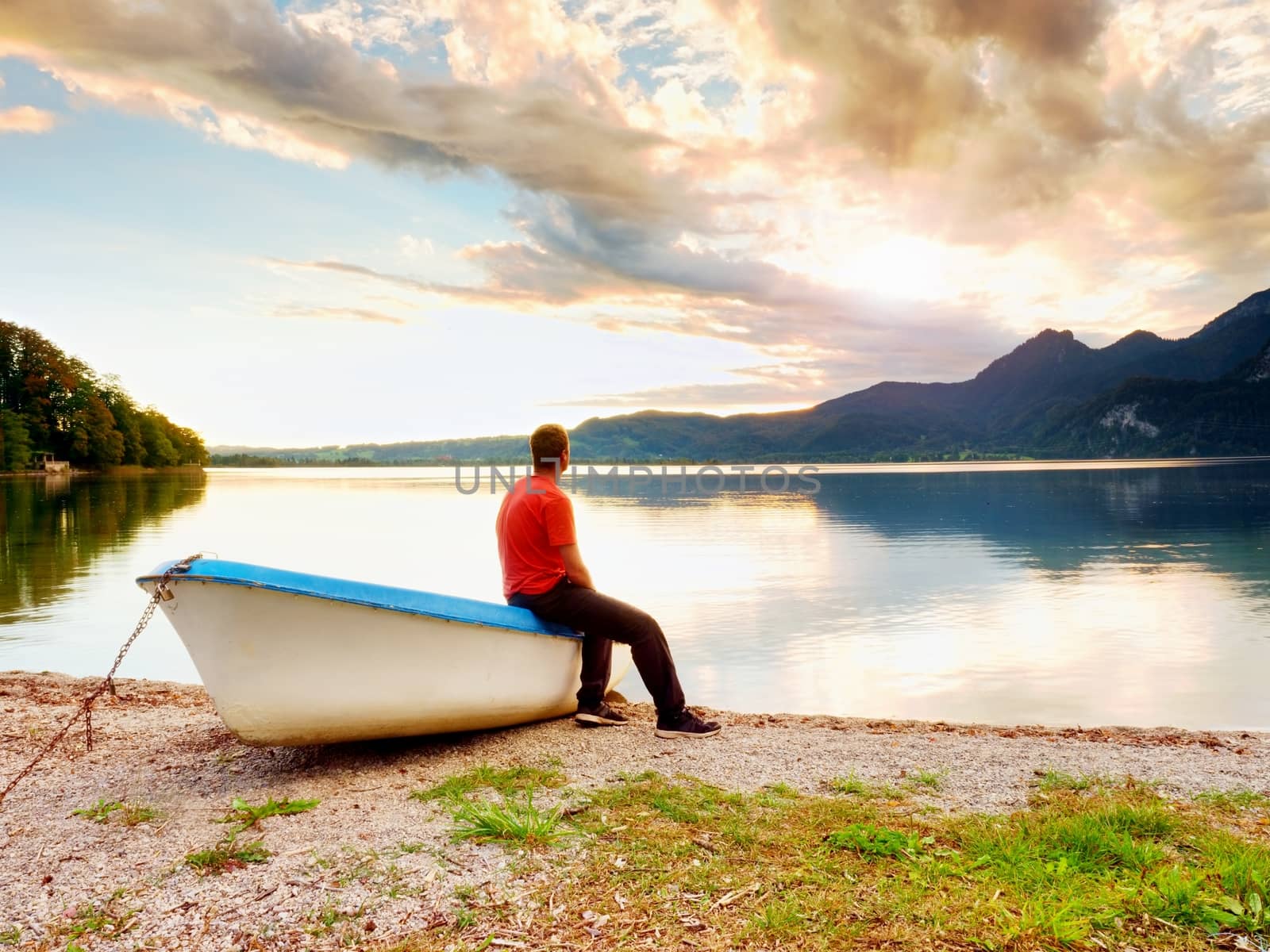 Tiired man in red shirt sit on old fishing paddle boat at mountains lake coast. by rdonar2