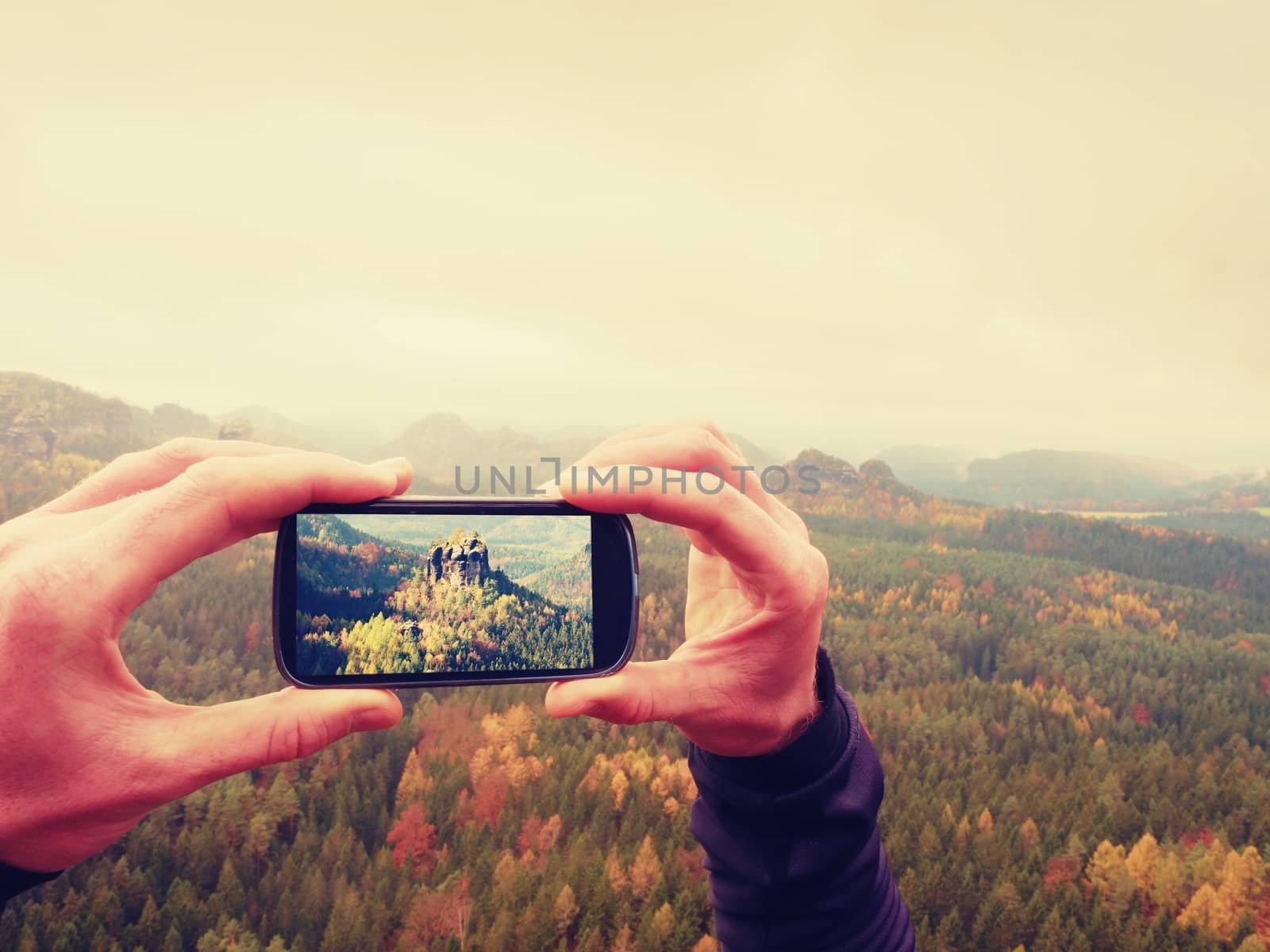 Smart phone mobile photography of misty spring mountains landscape. Focus to detail with phone in man hands. Long fingers keep frame of display.