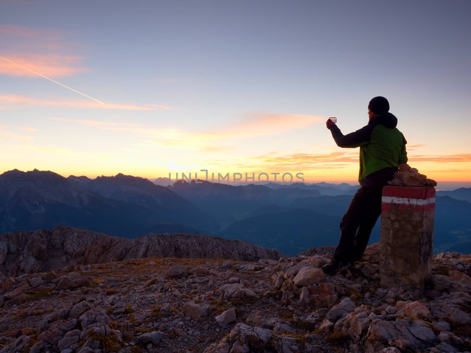 Hiker takes selfie photo. Man  sit on Austria Germany border stone on Alpine mountain. . Daybreak horizon above blue foggy valley. Mountains increased from humidity