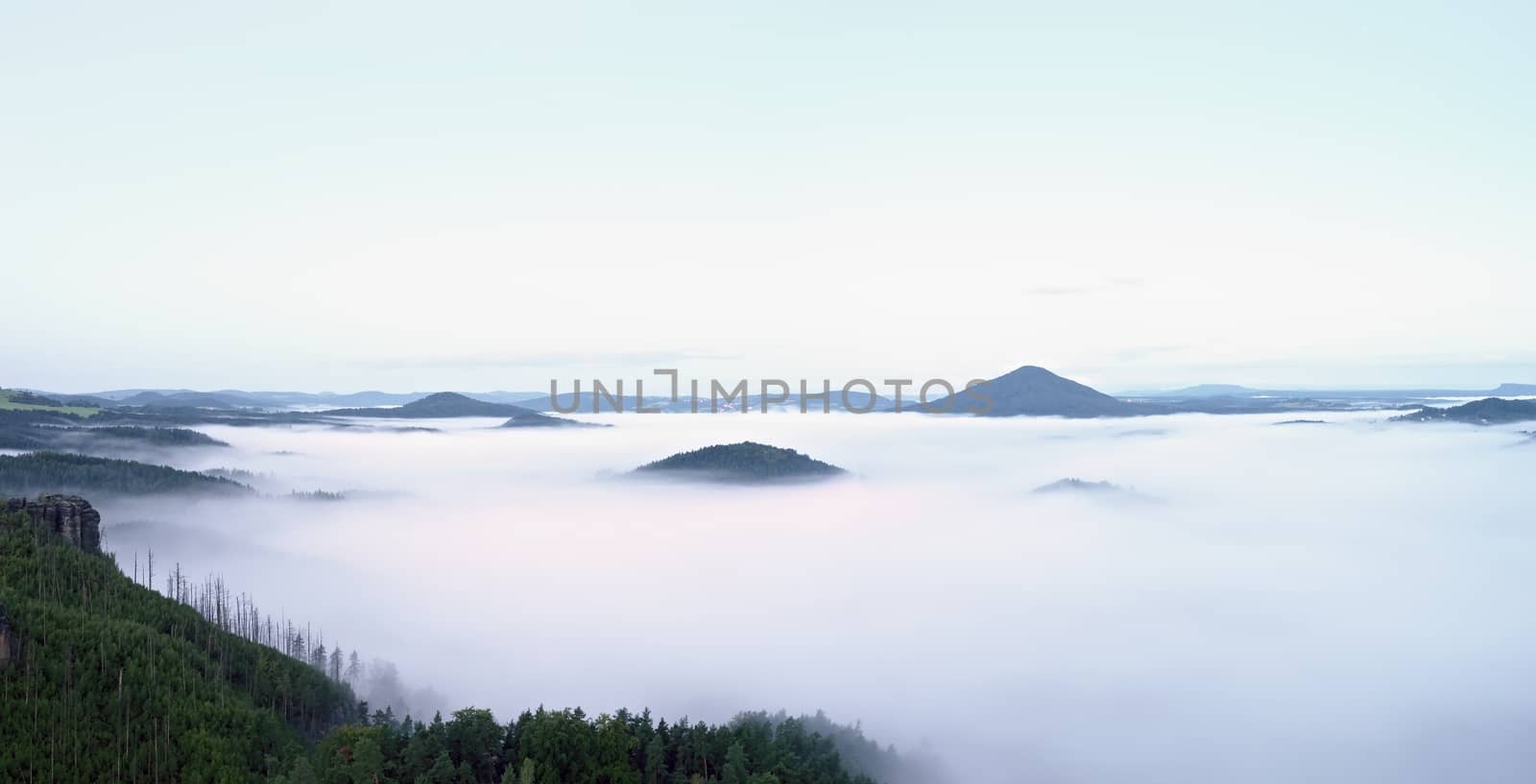 Magnificent heavy mist in landscape. Autumn creamy fog in countryside. Hill increased from fog, the fog is colored to gold and blue