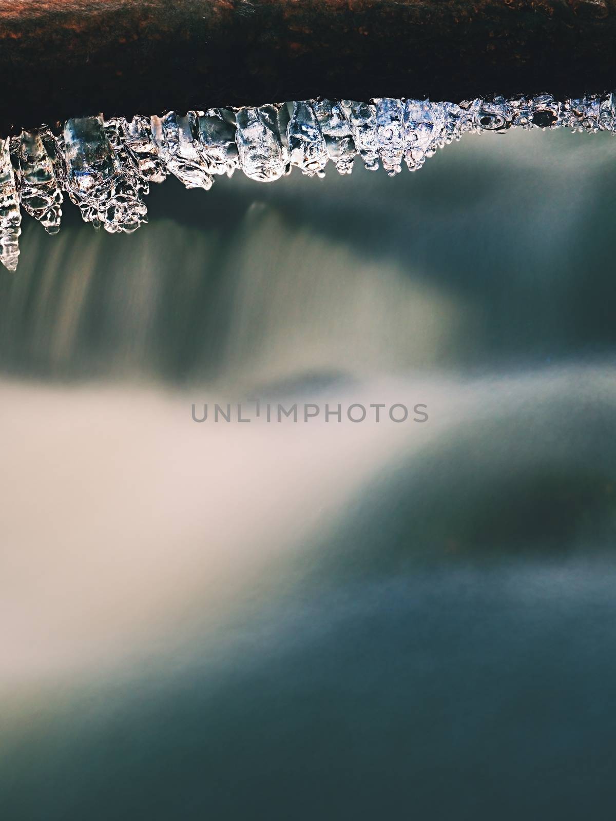 Long icicles hang above dark freeze  water of mountain stream. by rdonar2