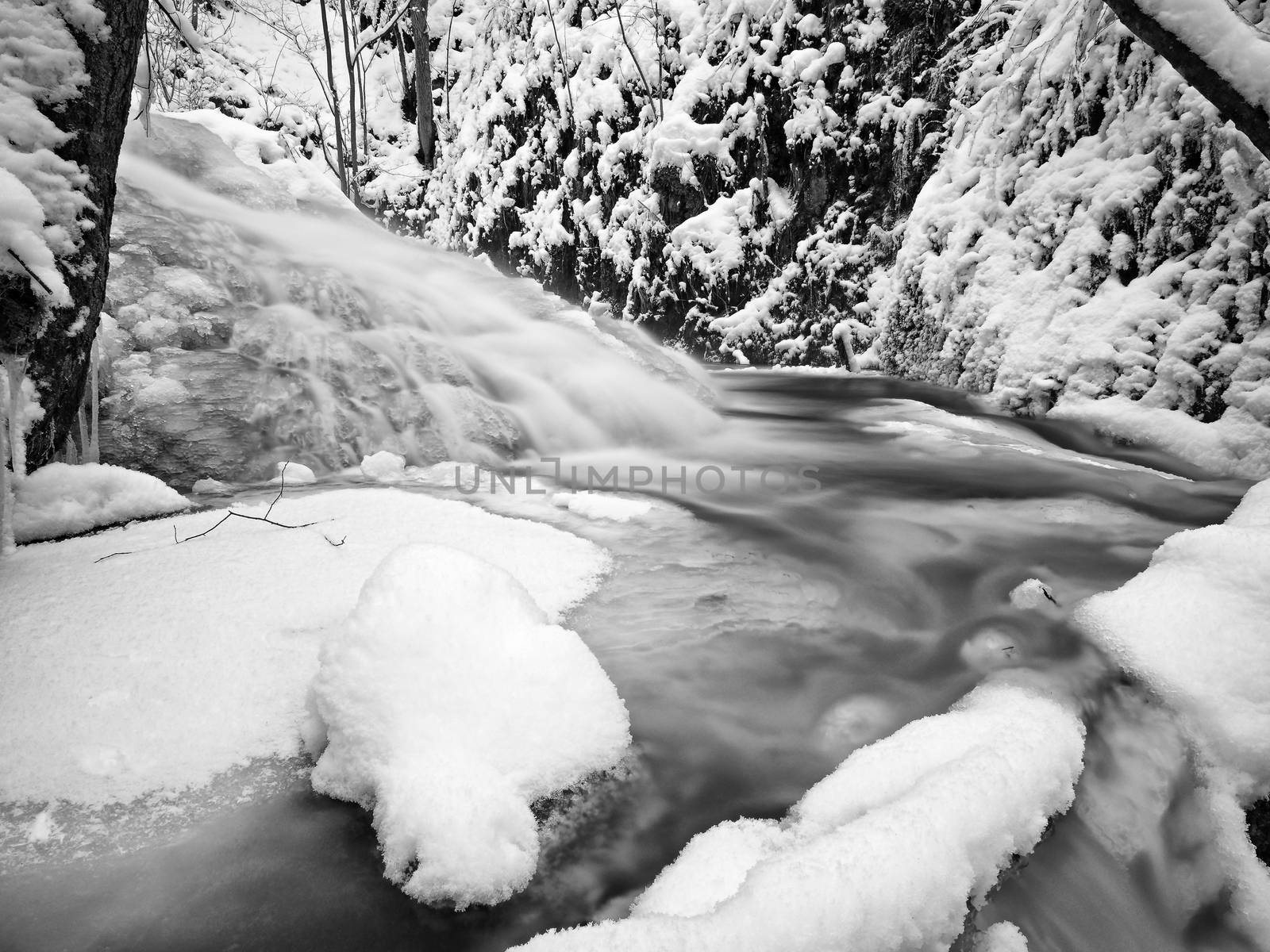 Frozen cascade of waterfall, icy twigs and icy boulders in frozen foam of rapid stream. Winter creek. Extreme freeze.