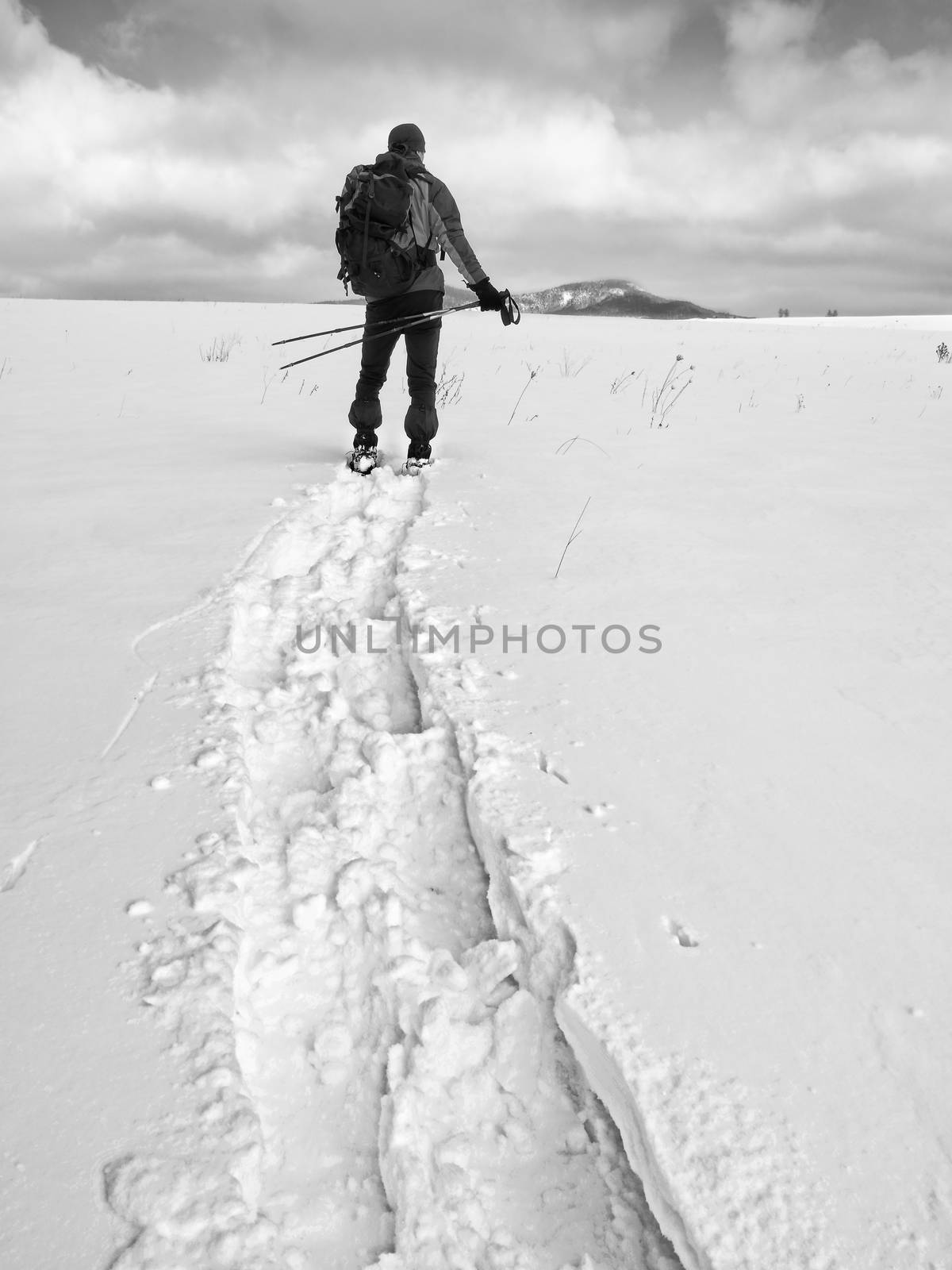 Hiker with backpack snowshoeing  in deep drift. Man with snowshoes walk in hill. Hiker in green gray winter jacket and black trekking trousers snowshoeing in powder snow.