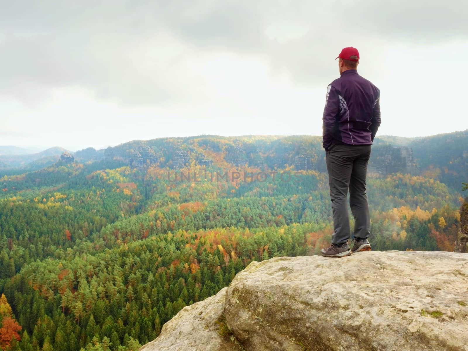 Hiker on rock end above valley. Man watch over misty and autumnal morning valley to bright morning Sun. Tourist  looking to misty valley bellow. Autumn cold weather