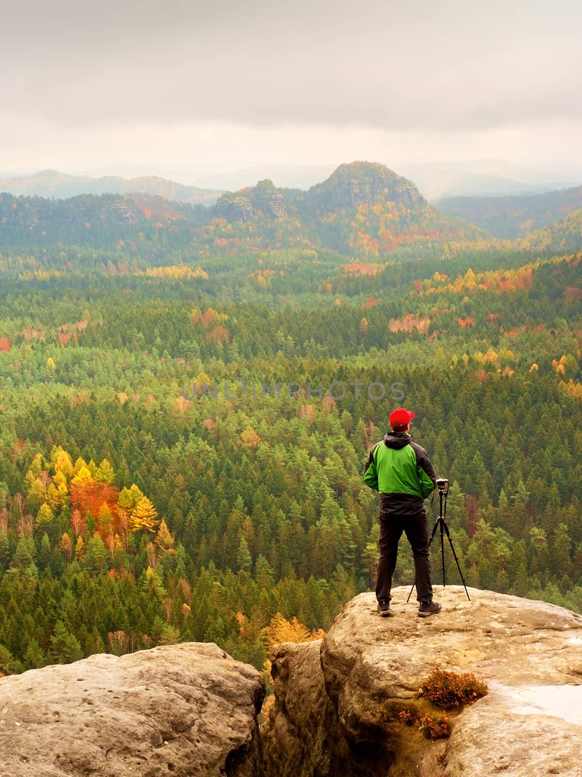 Tall adult  photographer prepare camera for taking picture of fall  mountains. Photograph at daybreak above  colorful  valley. Landscape view of autumn mountain hills and hiker above