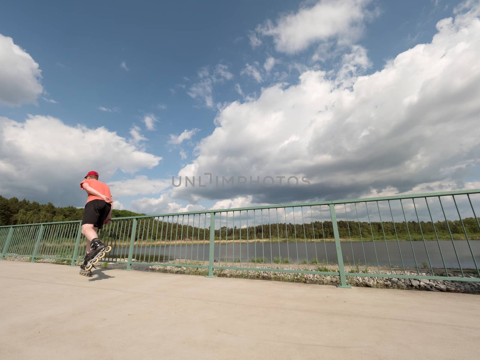 Roller skater in action. Man ride in inline skates ride along promenade handrail, blue sky in background. Low angle view