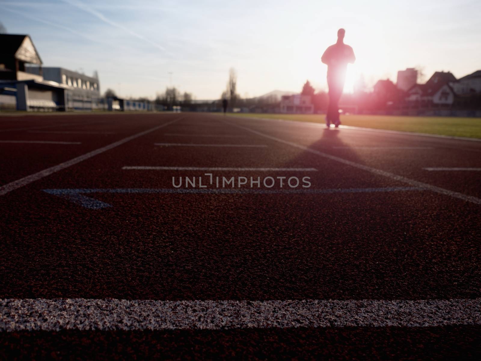 Tall man running on red running racetrack on the stadium. Sportsman in training clothes at amazing sunset. Sport and healthy lifestyle concept and jogging civic training workout