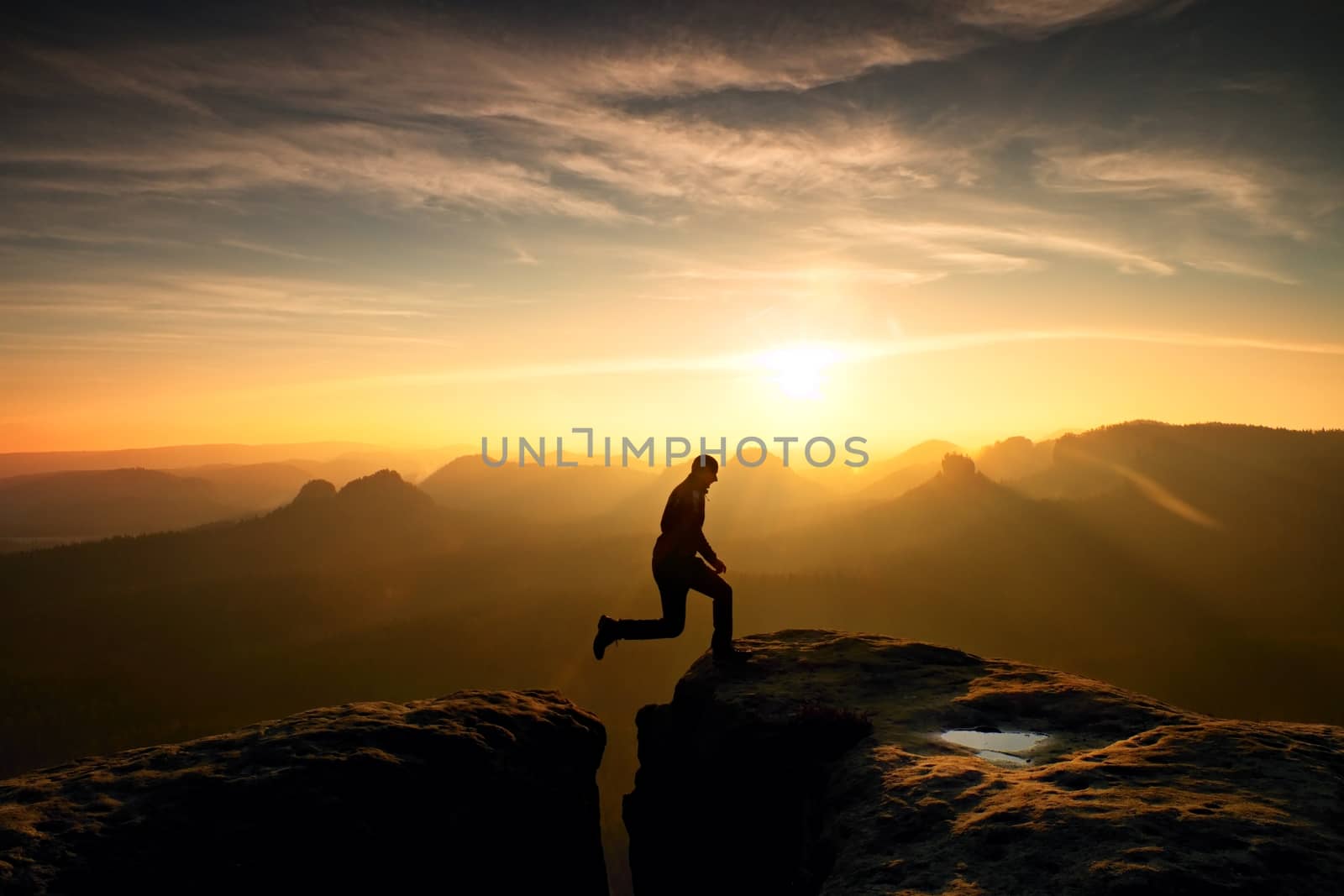 Jumping man. Young man makes jump on colorful sky background in mountains. heavy orange mist in deep valley. Miracle of nature