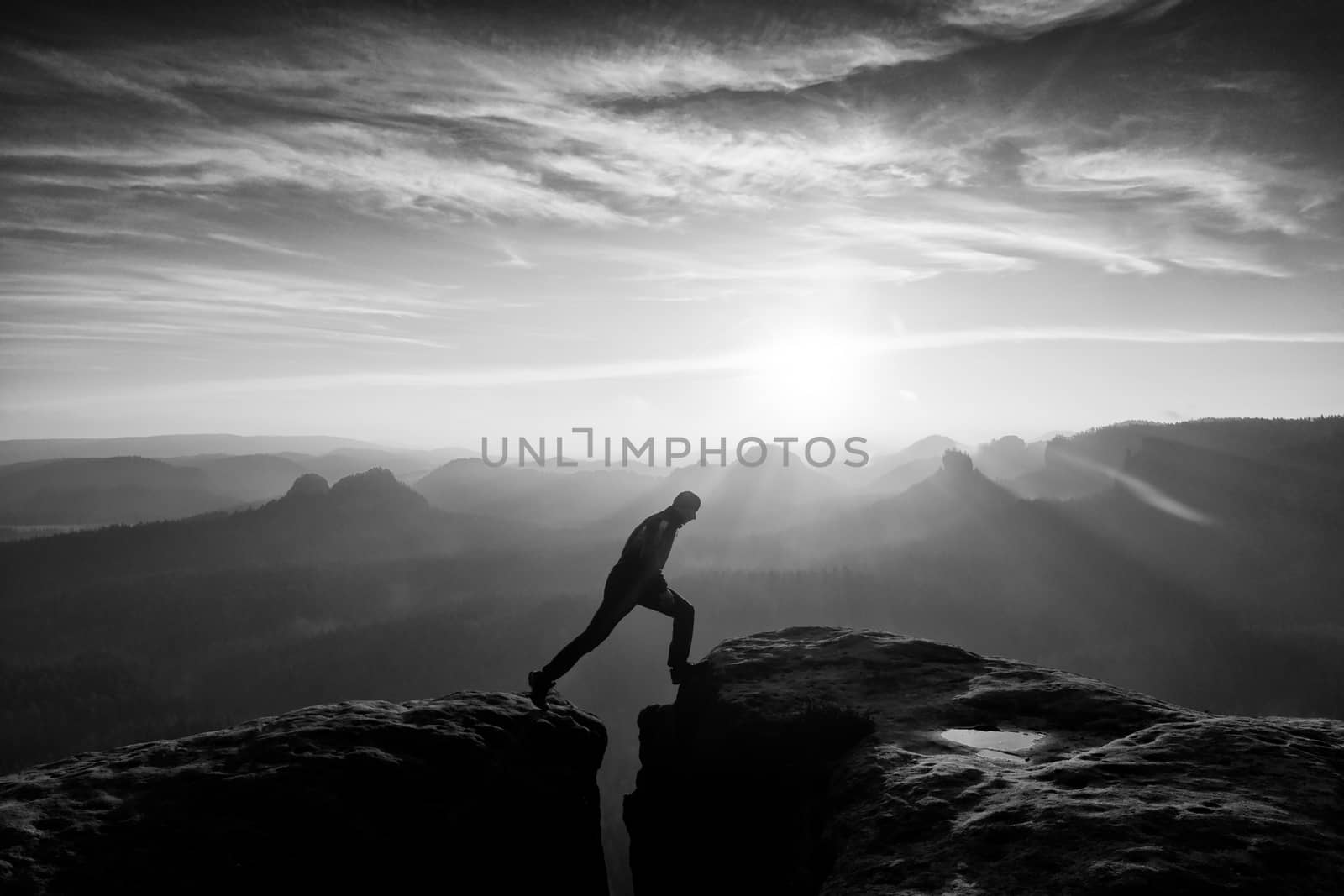 Jumping man. Young man makes jump on colorful sky background in mountains. heavy orange mist in deep valley. Miracle of nature