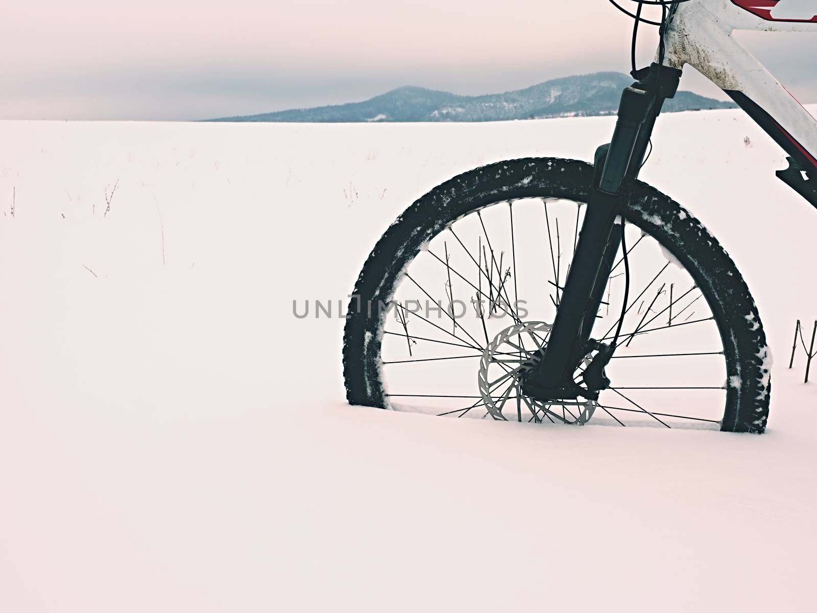 The front wheel of mountain bike stay in powder snow. Lost path under deep snowdrift. Snow flakes melting on dark off road tyre.  Winter weather in the field.