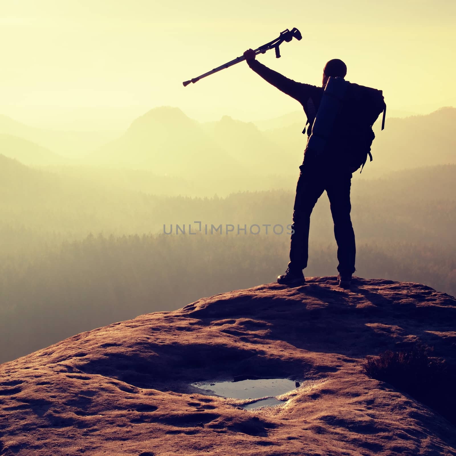 Hiker with medicine crutch above head achieved mountain peak. Broken leg fixed in immobilizer Deep misty valley bellow silhouette of man with hand in air. Spring daybreak