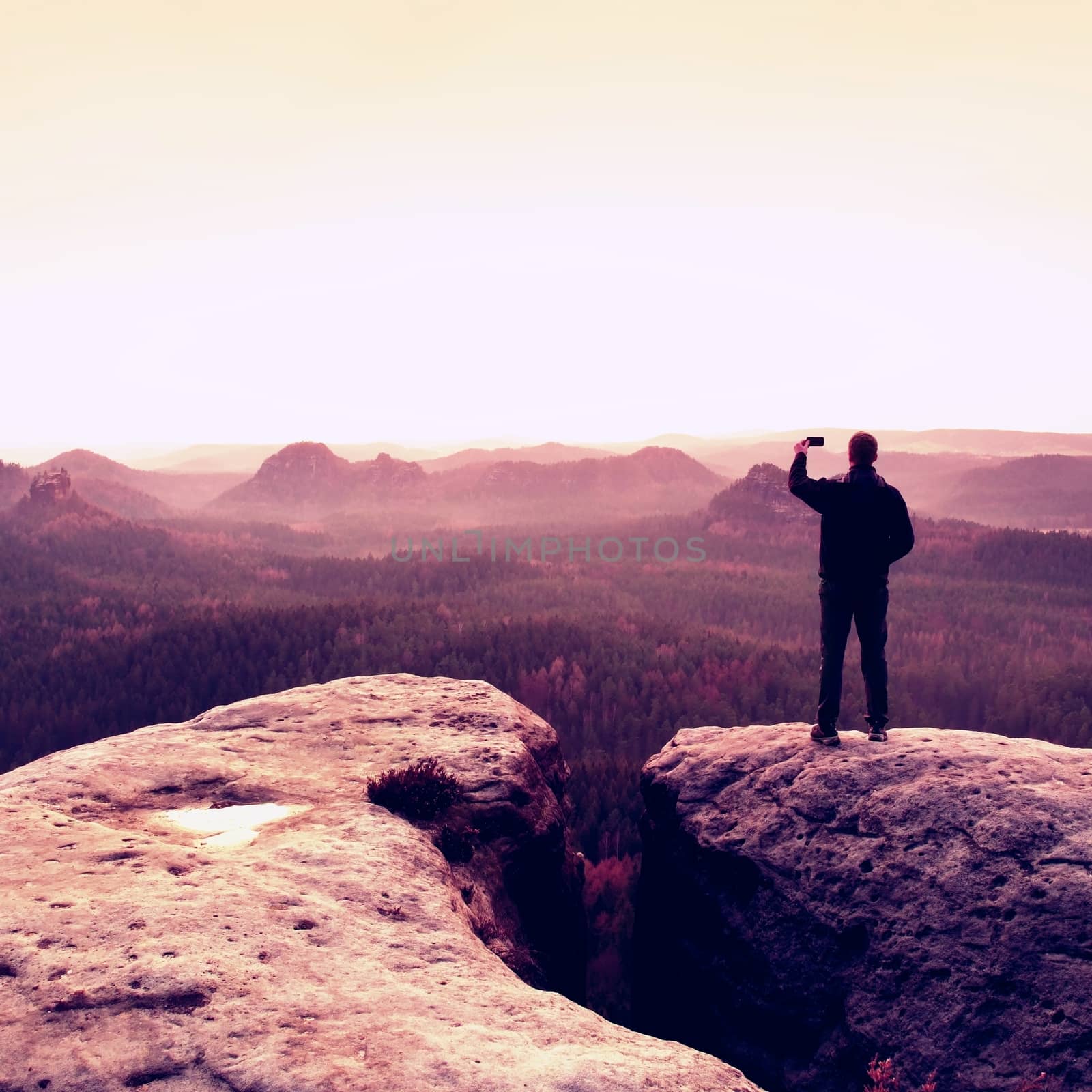 Man photography with phoneof  dreamy hilly landscape, spring orange pink misty sunrise in a beautiful valley of rocky mountains.