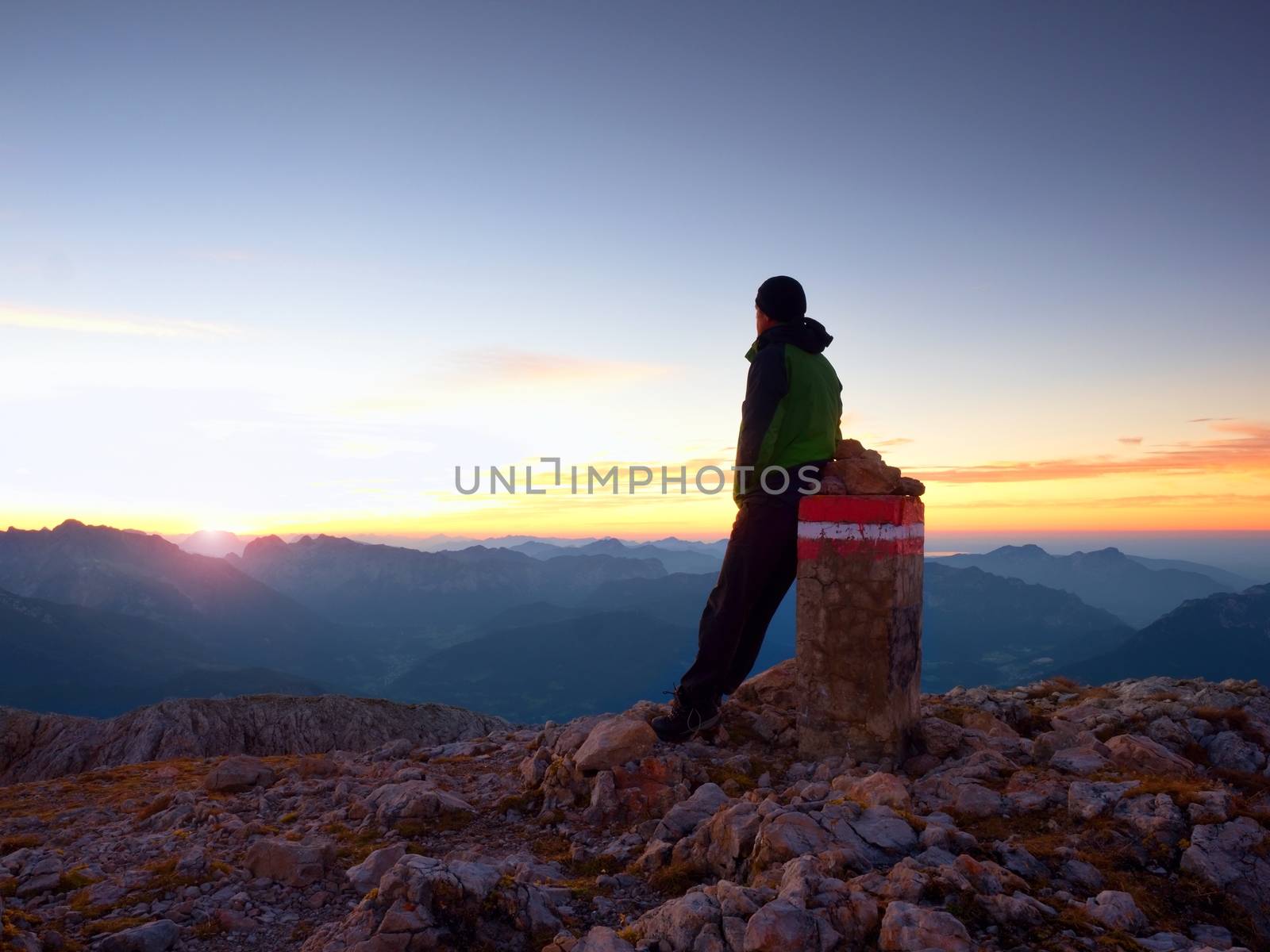 Tired hiker sit on border stone on Alps mountain. Austria Germany border. Daybreak above foggy valley by rdonar2